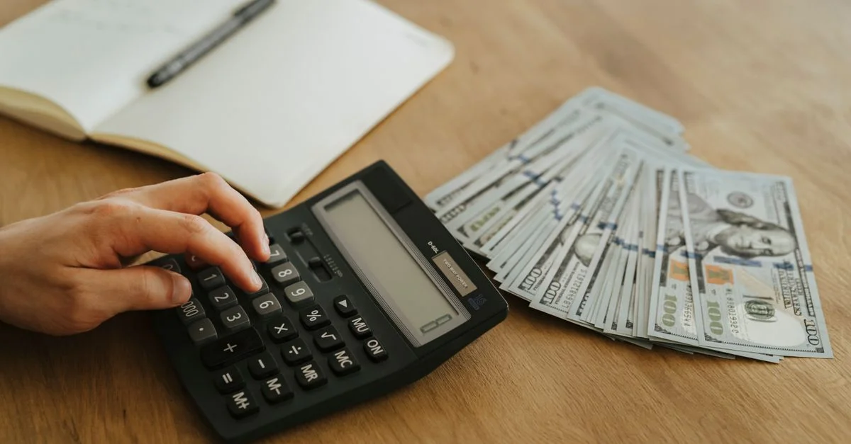 Gros plan sur une main utilisant une calculatrice avec de l'argent liquide et un carnet sur une table en bois.