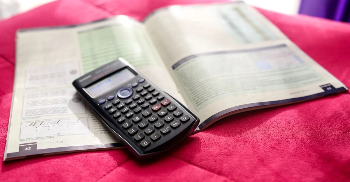 Une calculatrice scientifique et un manuel ouvert sur une surface rose vibrante, idéale pour des thèmes éducatifs et académiques.
