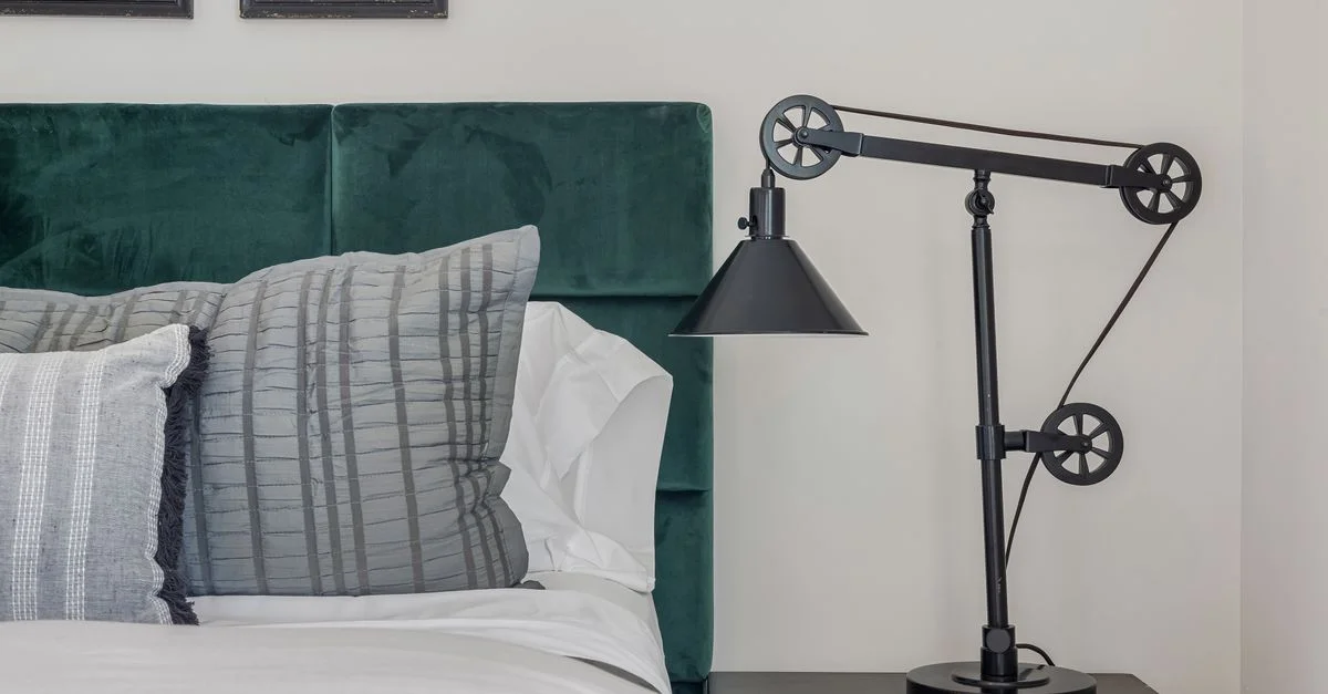 Chambre élégante avec une lampe contemporaine, une tête de lit en velours et des coussins moelleux.
