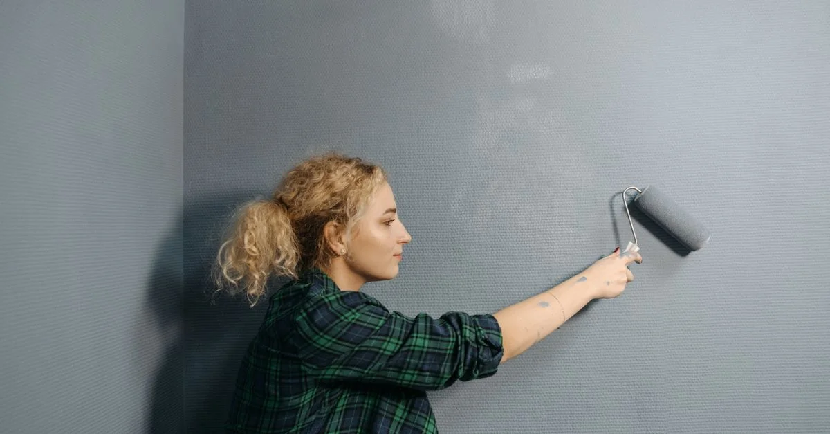 Jeune femme utilise un rouleau à peinture pour appliquer de la peinture grise sur un mur intérieur, rénovant son espace.