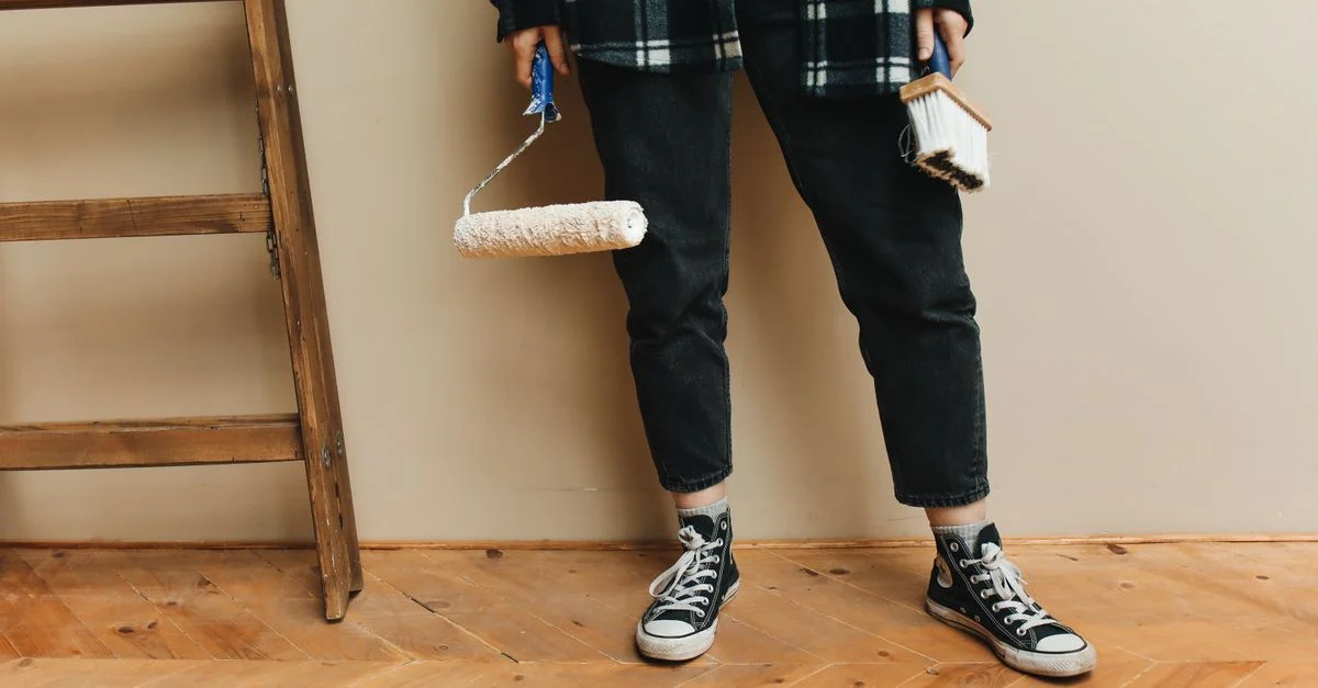 Une personne tenant un rouleau de peinture et un pinceau lors d'un projet de rénovation domiciliaire.
