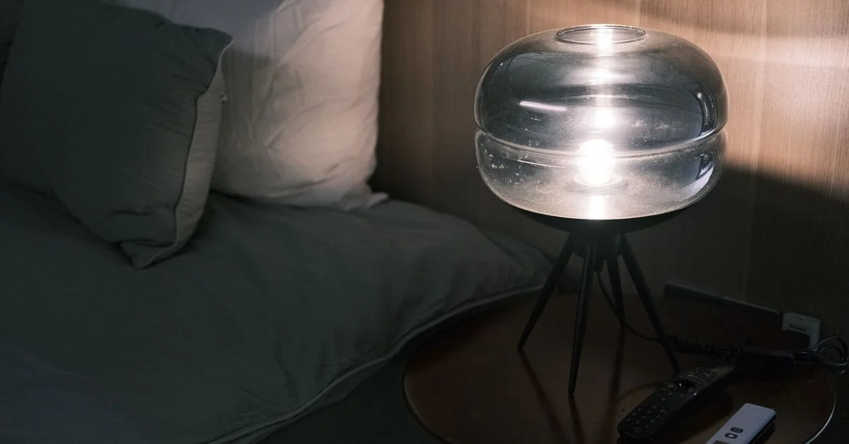 Table de chevet illuminée avec une lampe moderne en verre et des oreillers la nuit.