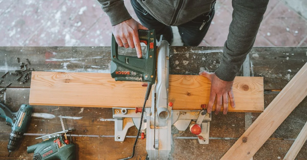 Un menuisier utilise une scie sauteuse électrique sur une planche de bois, entouré d'outils.