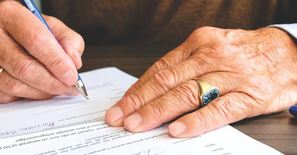 Gros plan d'un senior signant un document légal, mettant l'accent sur la main et l'alliance en or.