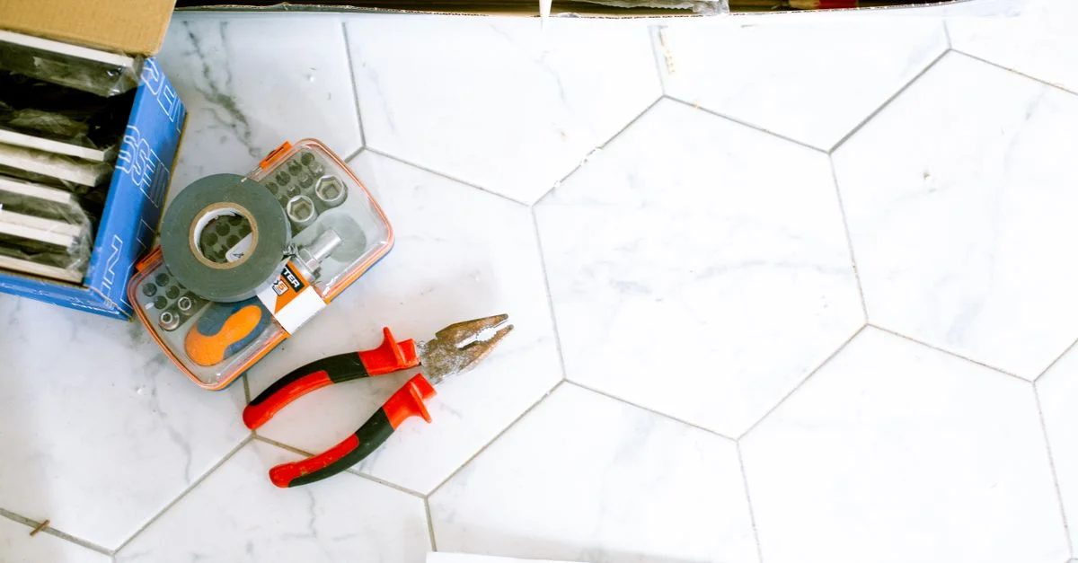 Une sélection d'outils de rénovation domiciliaire posée sur un sol en carreaux blancs, prête à être utilisée.